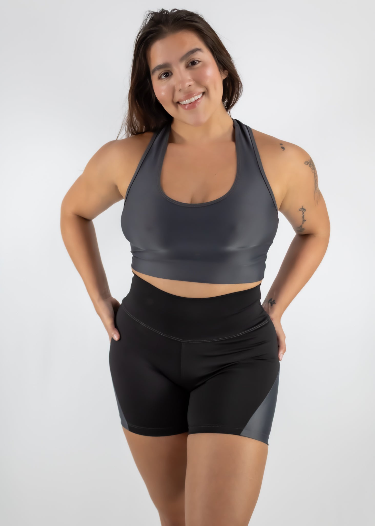 Woman wearing a gray sports bra and black shorts on a white background