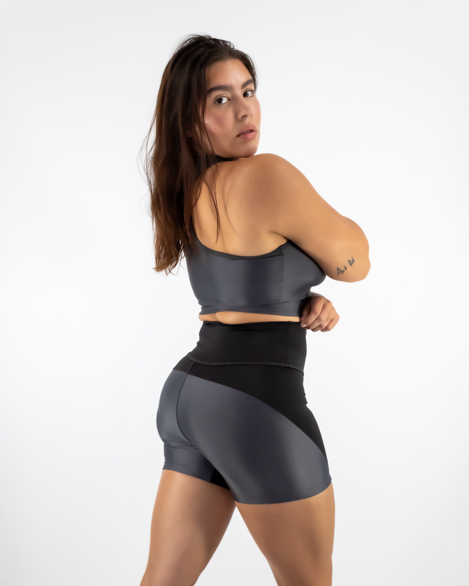 Woman wearing a gray sports bra and black shorts on a white background