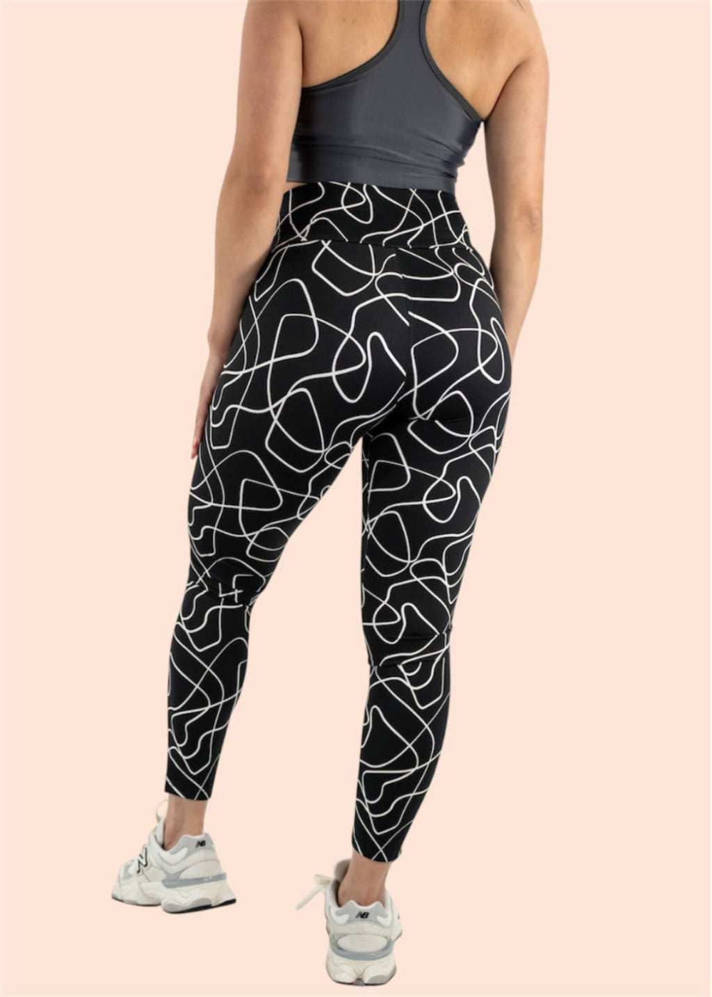 Person wearing black leggings with white abstract patterns on a beige background