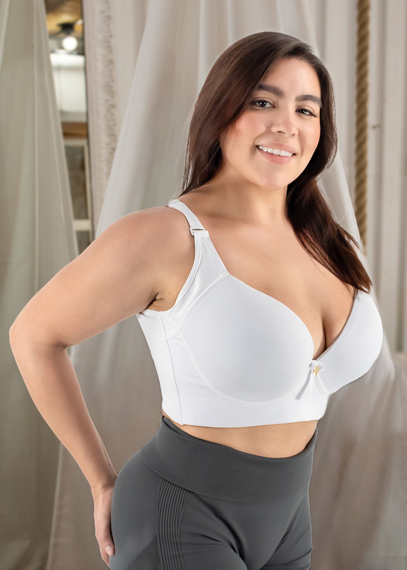 Woman wearing a white sports bra and gray leggings indoors.