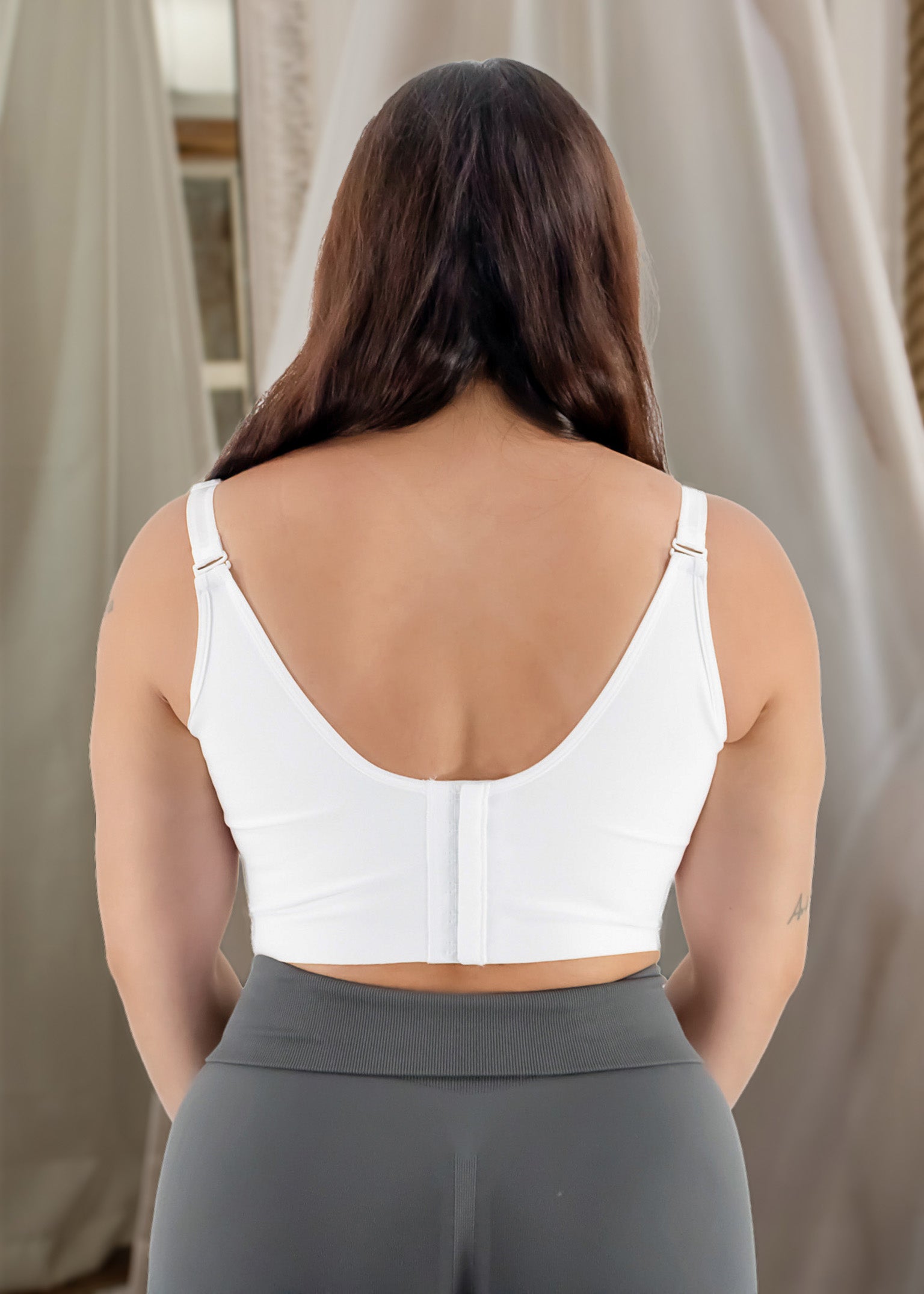 Person wearing a white sports bra and gray leggings against a neutral background