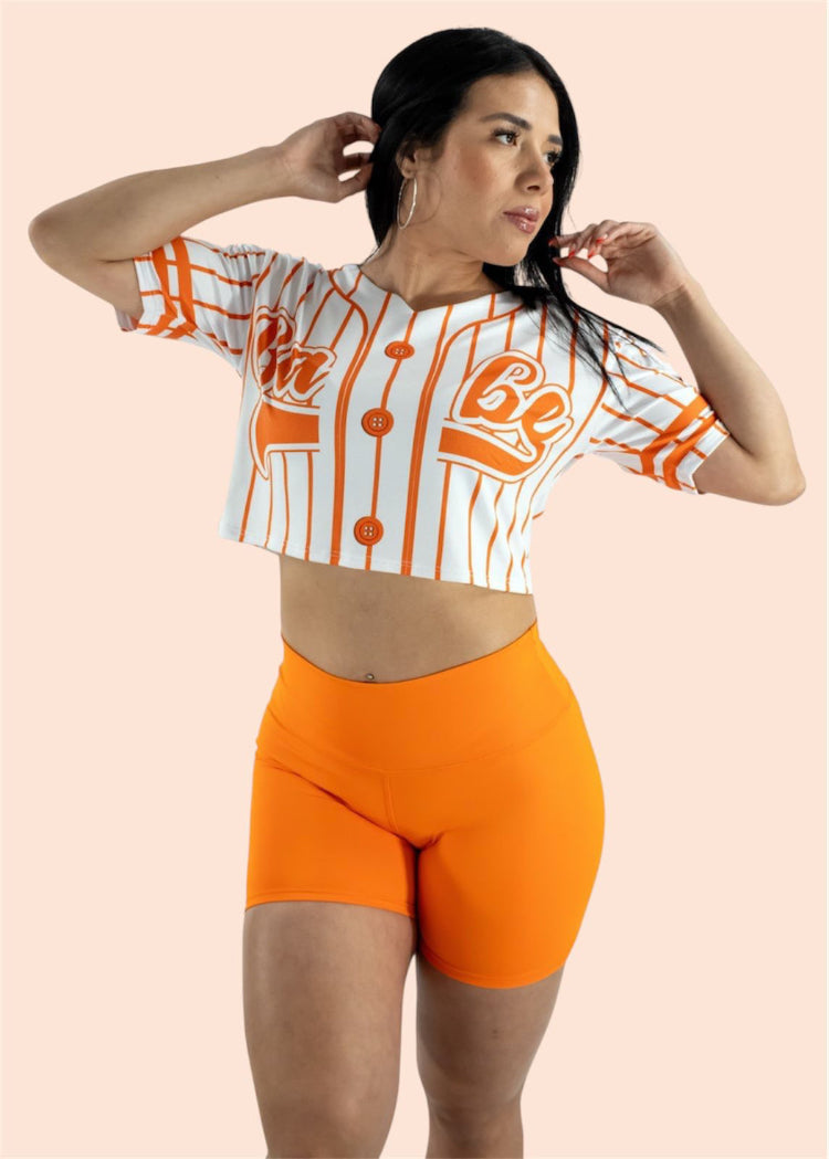 Woman wearing a sports jersey and orange shorts on a light pink background