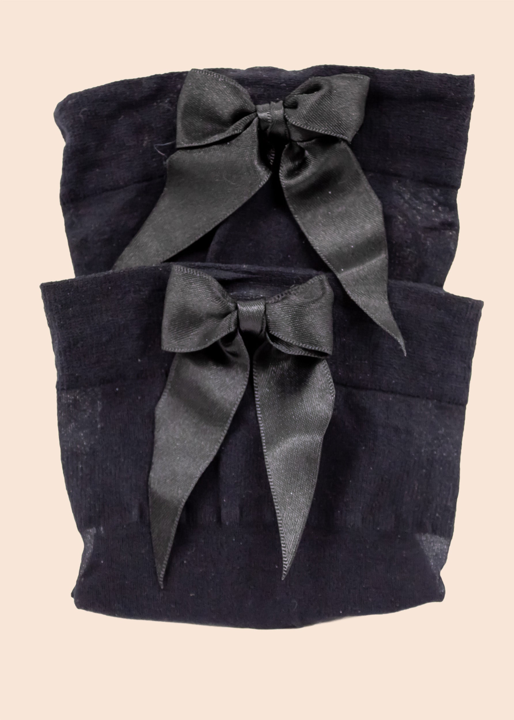 Two black fabric pouches with satin ribbons on a beige background