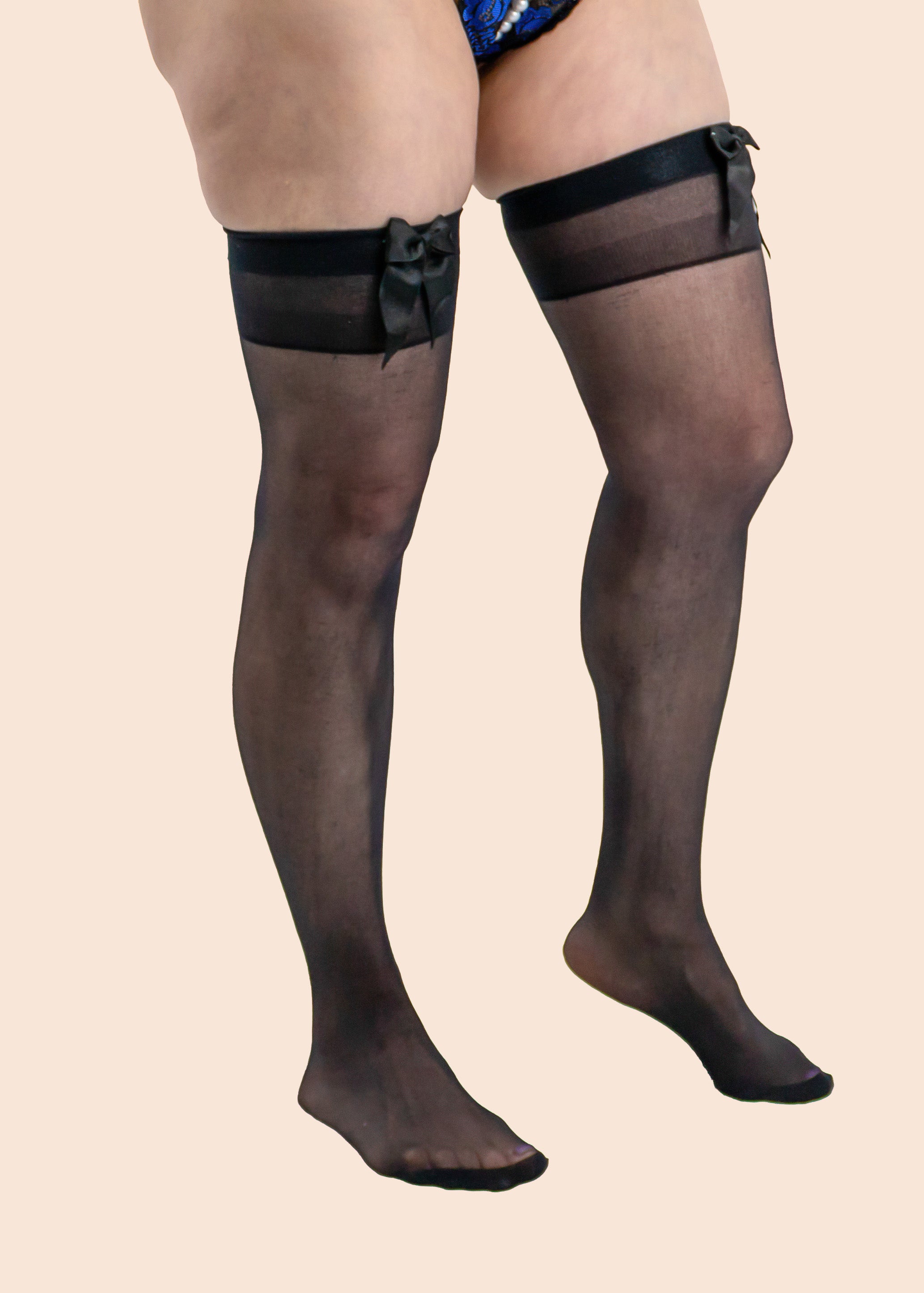 Black sheer stockings with garters worn by a person on a beige background