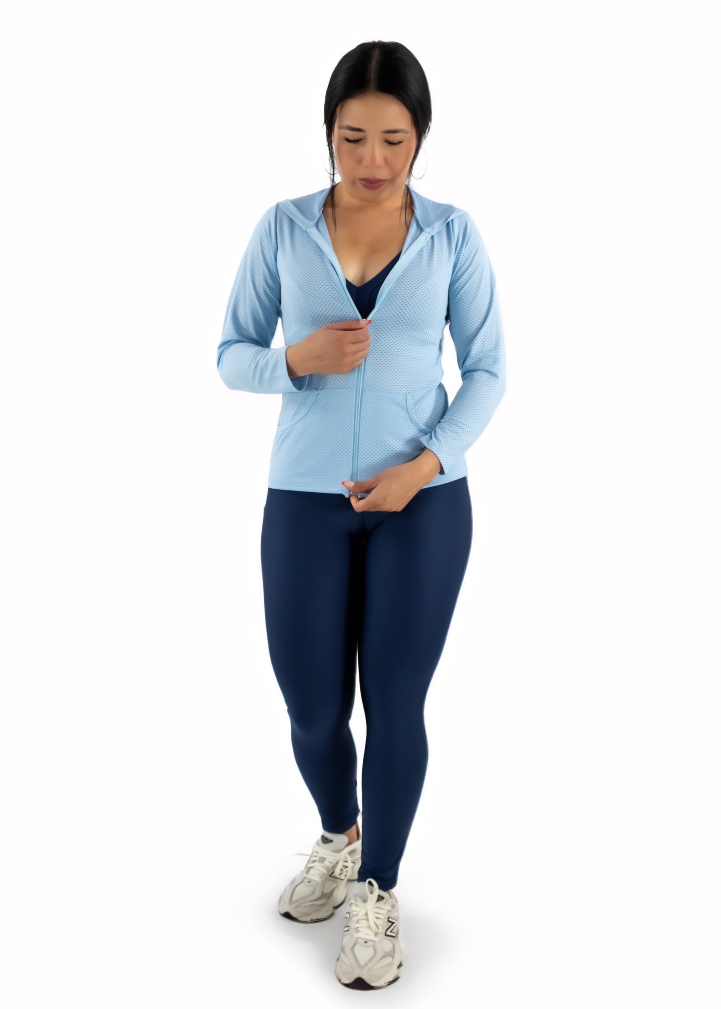 Woman wearing a light blue hoodie and dark blue leggings on a white background