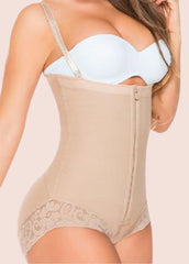 Woman wearing a beige shapewear garment with a white bra on a light pink background