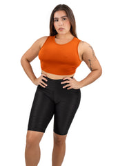 Woman wearing an orange crop top and black shorts on a white background