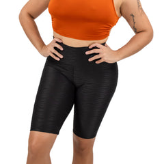 Woman wearing an orange crop top and black shorts on a white background