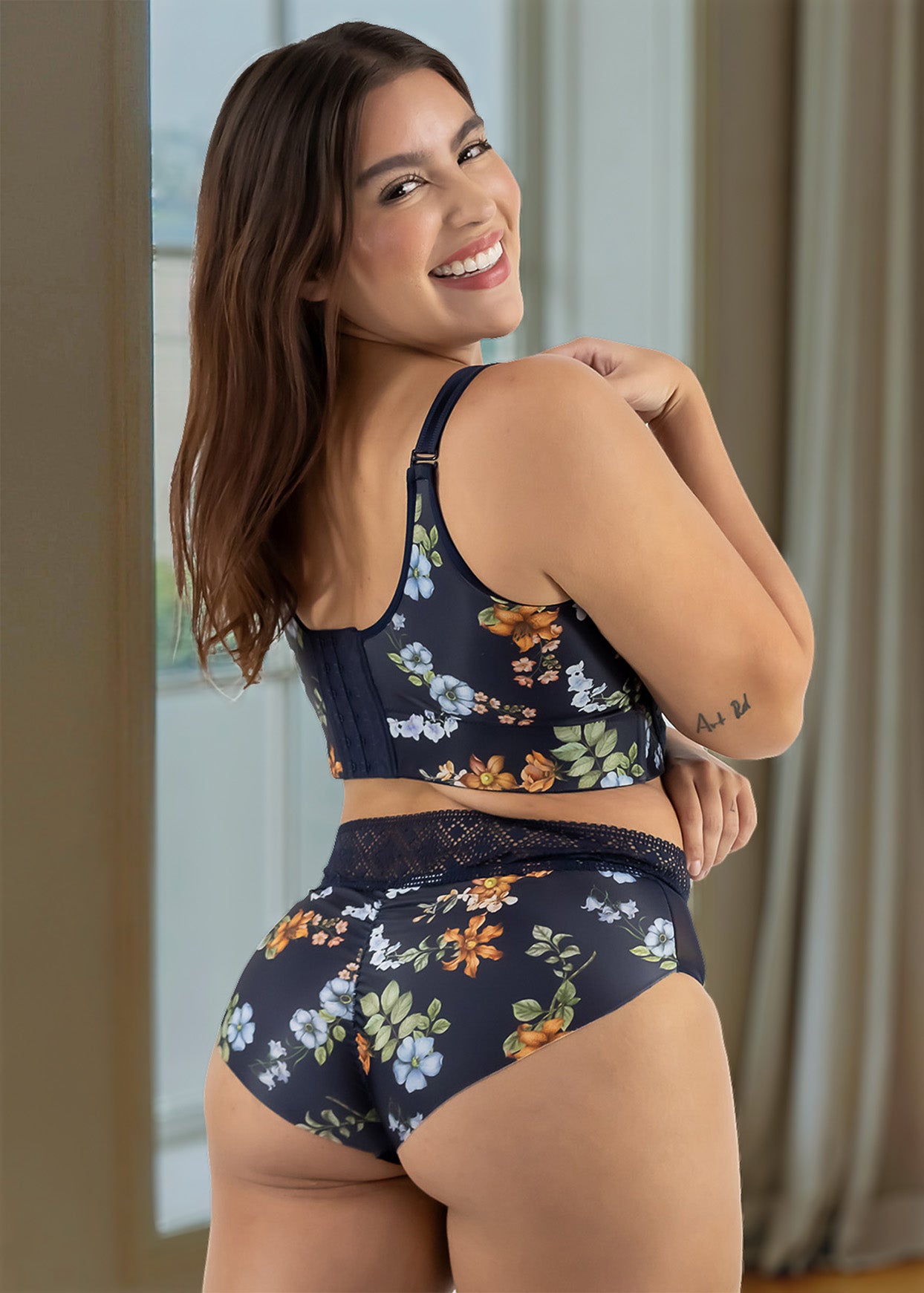 Woman wearing a floral lingerie set in a room with curtains.