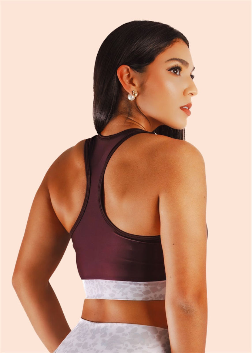 Woman wearing a dark brown sports bra with lace trim on a beige background