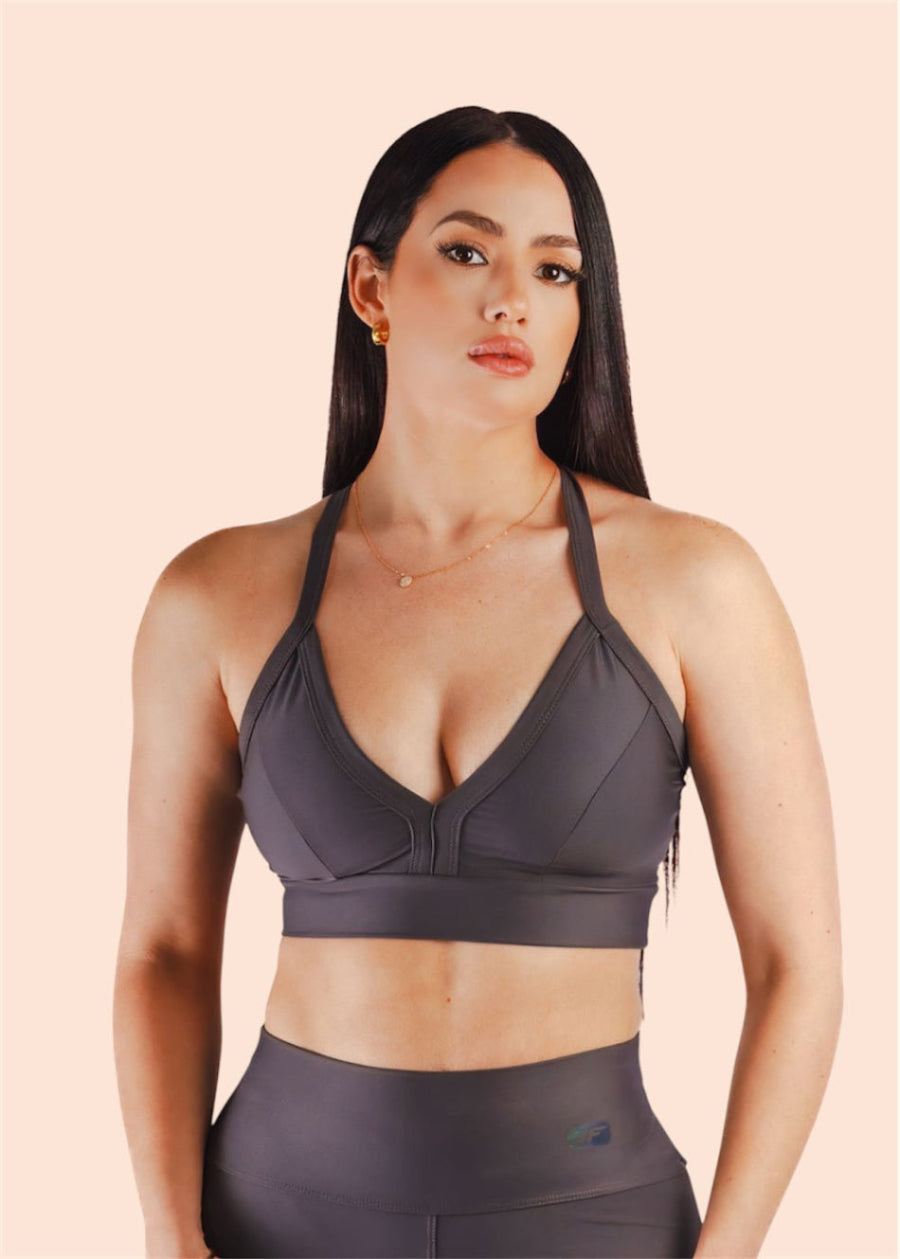Woman wearing a dark gray sports bra and leggings on a beige background