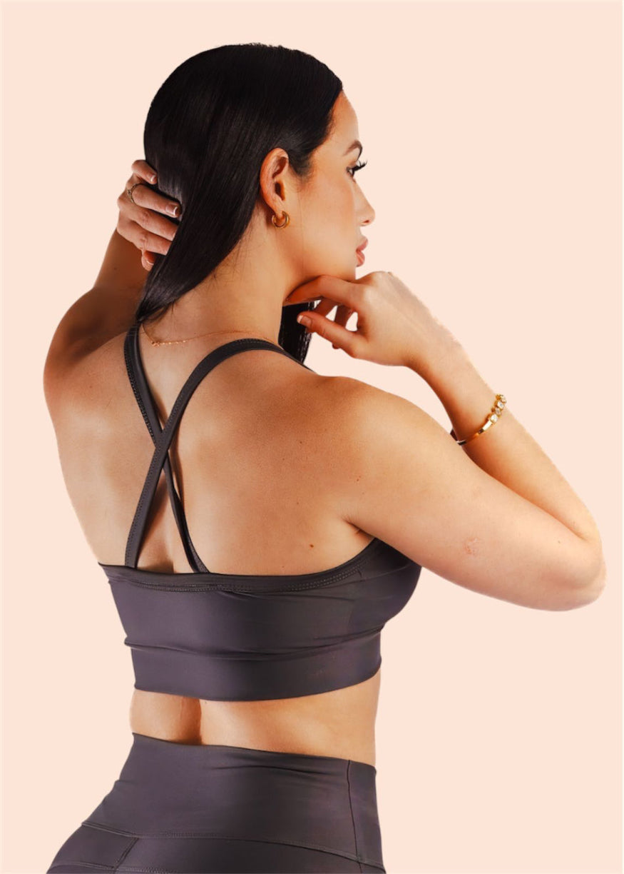 Woman wearing a dark gray sports bra and leggings on a light pink background