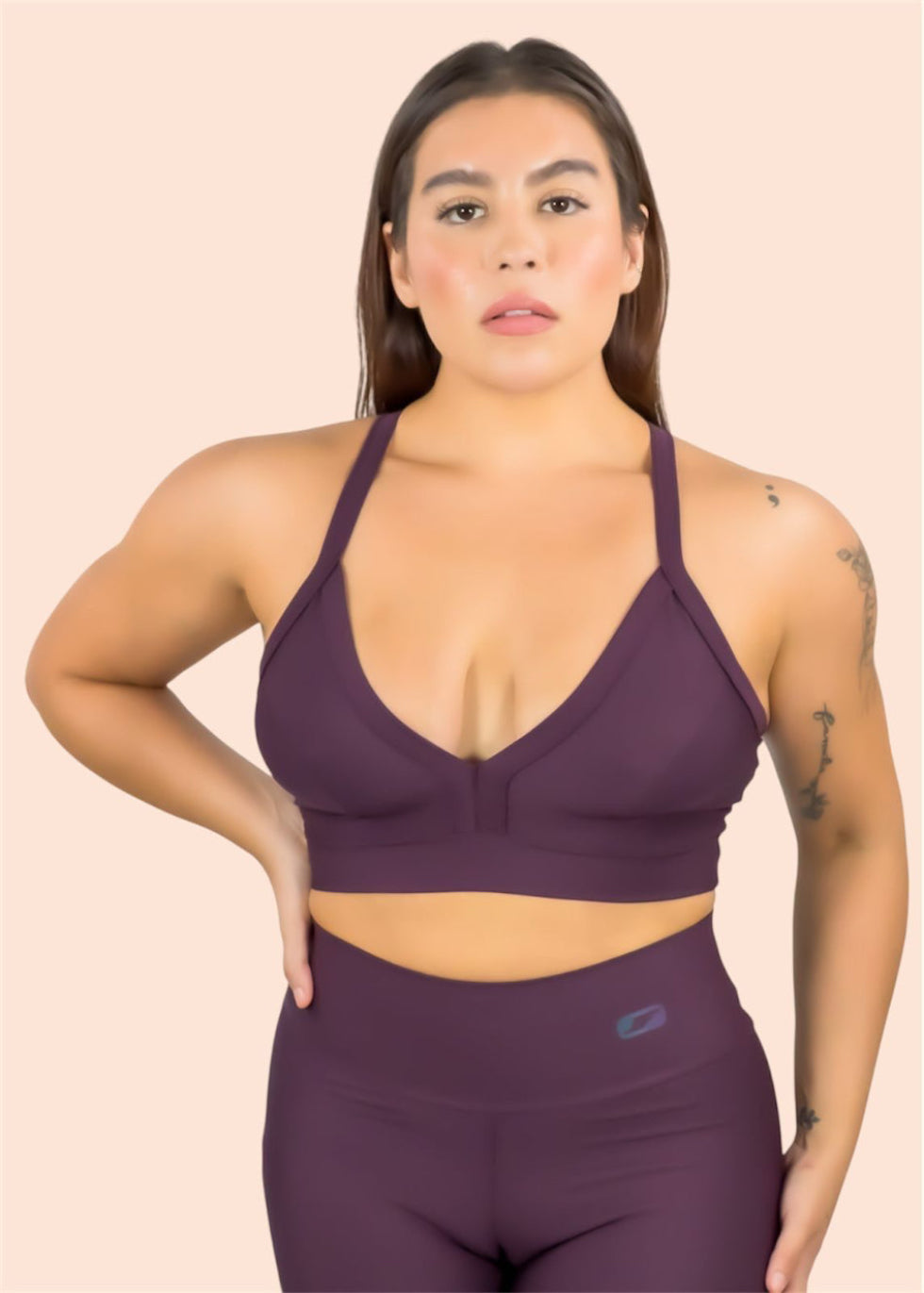 Woman wearing a purple sports bra and leggings set on a beige background