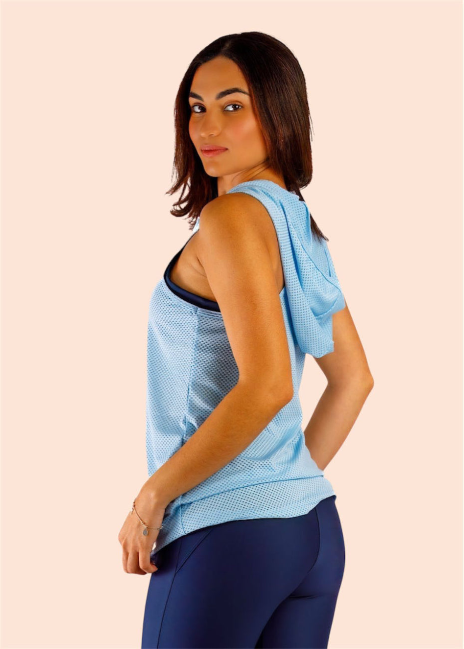 Woman wearing a light blue sleeveless top and dark blue leggings on a beige background