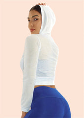 Woman wearing a white mesh long-sleeve crop top and blue leggings on a beige background