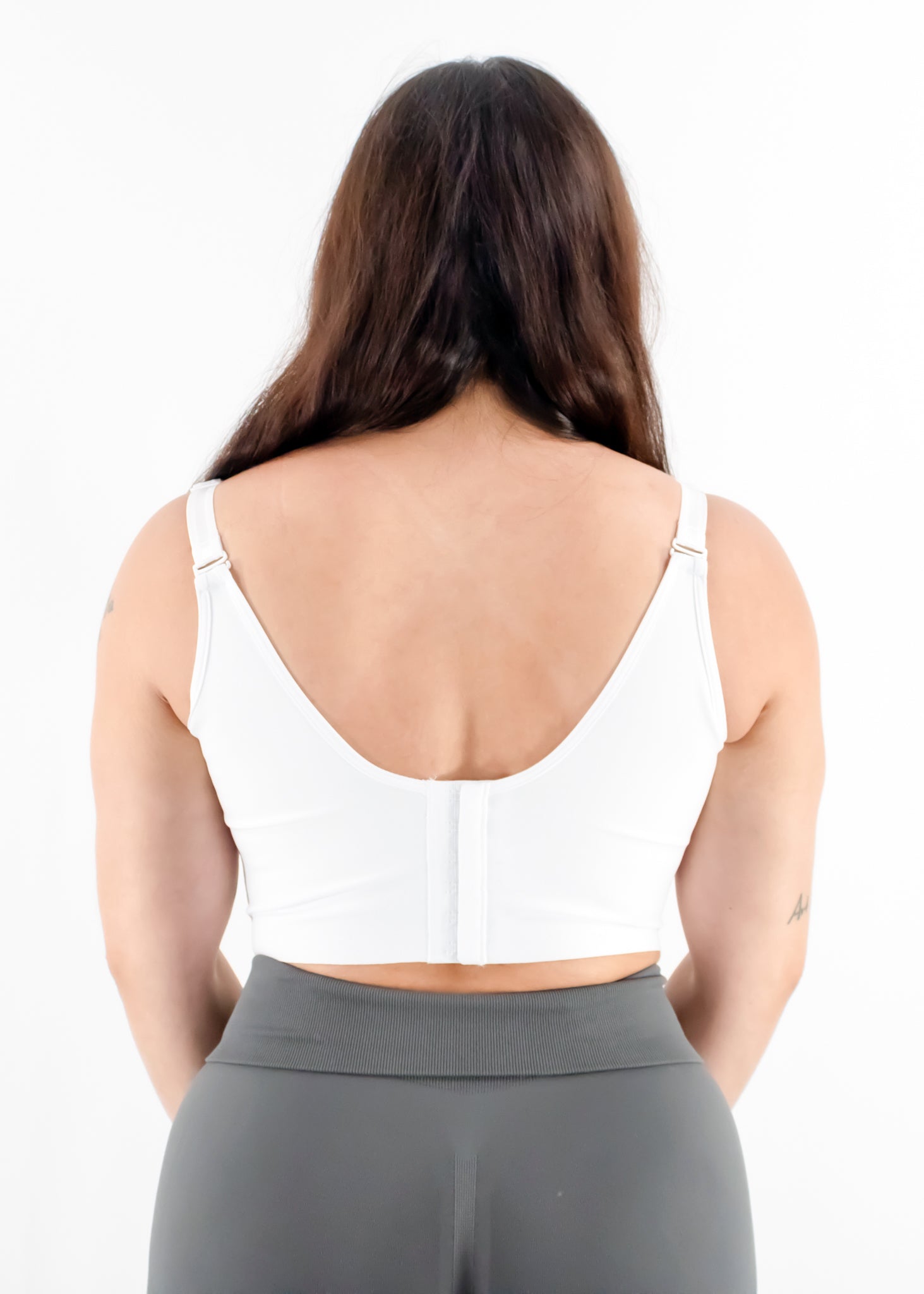 Woman wearing a white sports bra and gray leggings on a white background