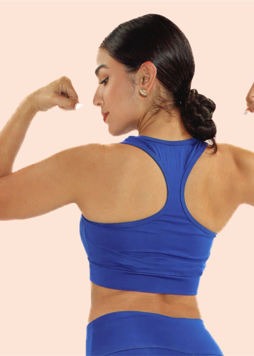 Woman in a blue sports bra and leggings flexing her muscles on a beige background