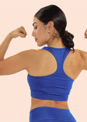 Woman in a blue sports bra and leggings flexing her muscles on a beige background