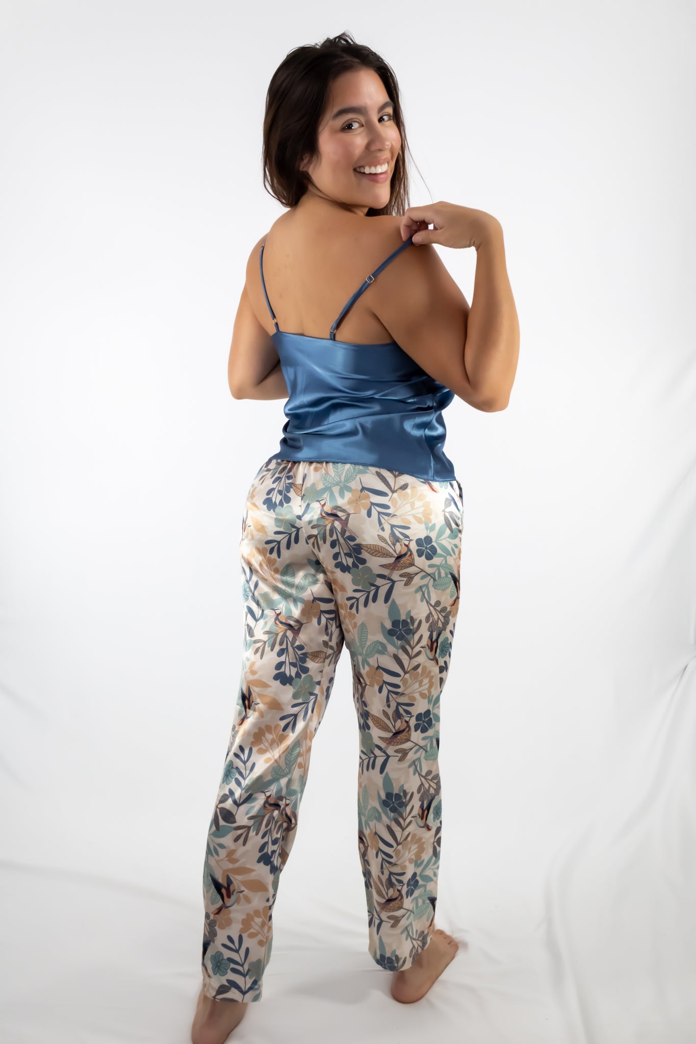 Woman wearing a blue satin top and floral pants on a white background