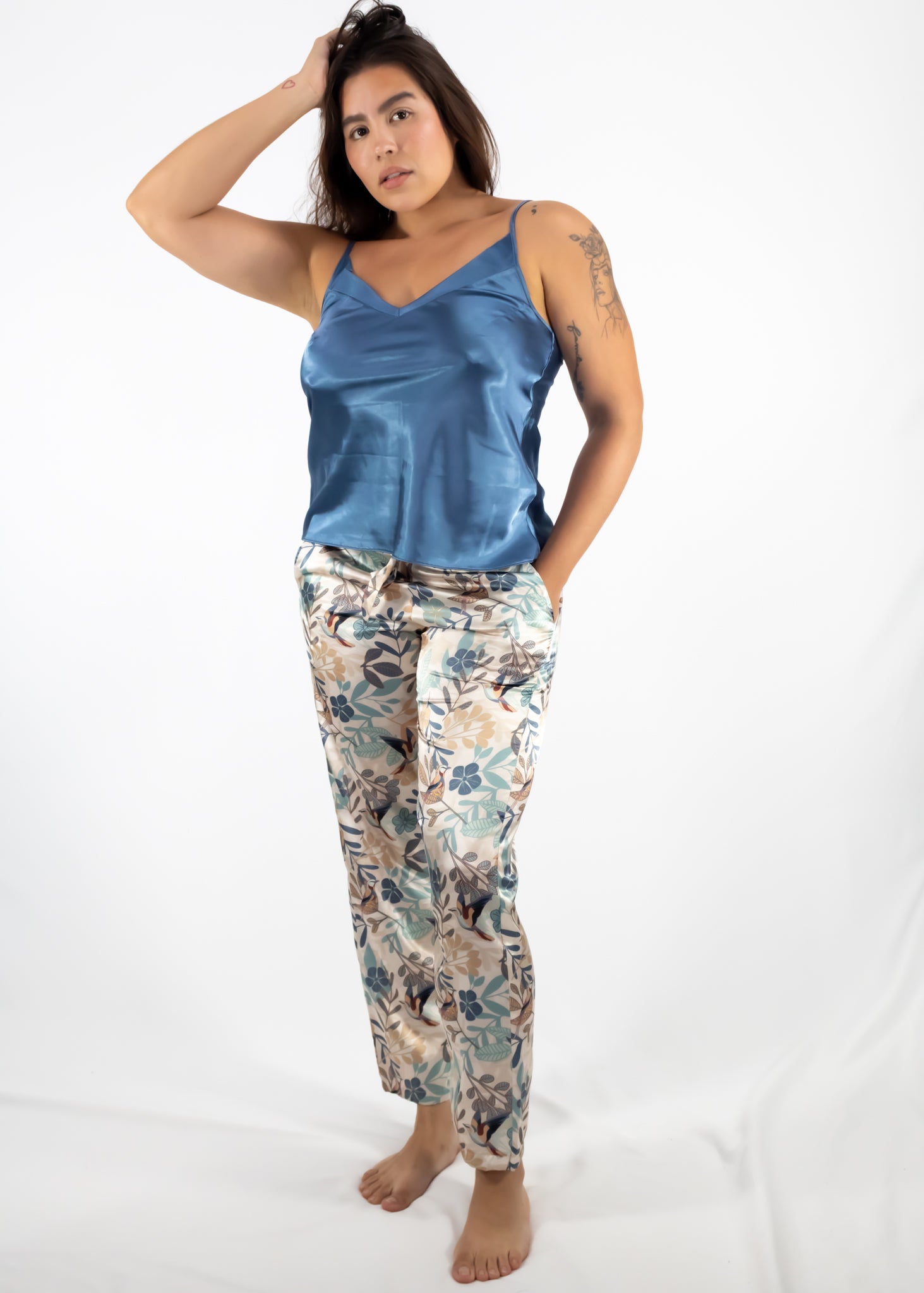 Woman wearing a blue satin tank top and floral pajama pants on a white background