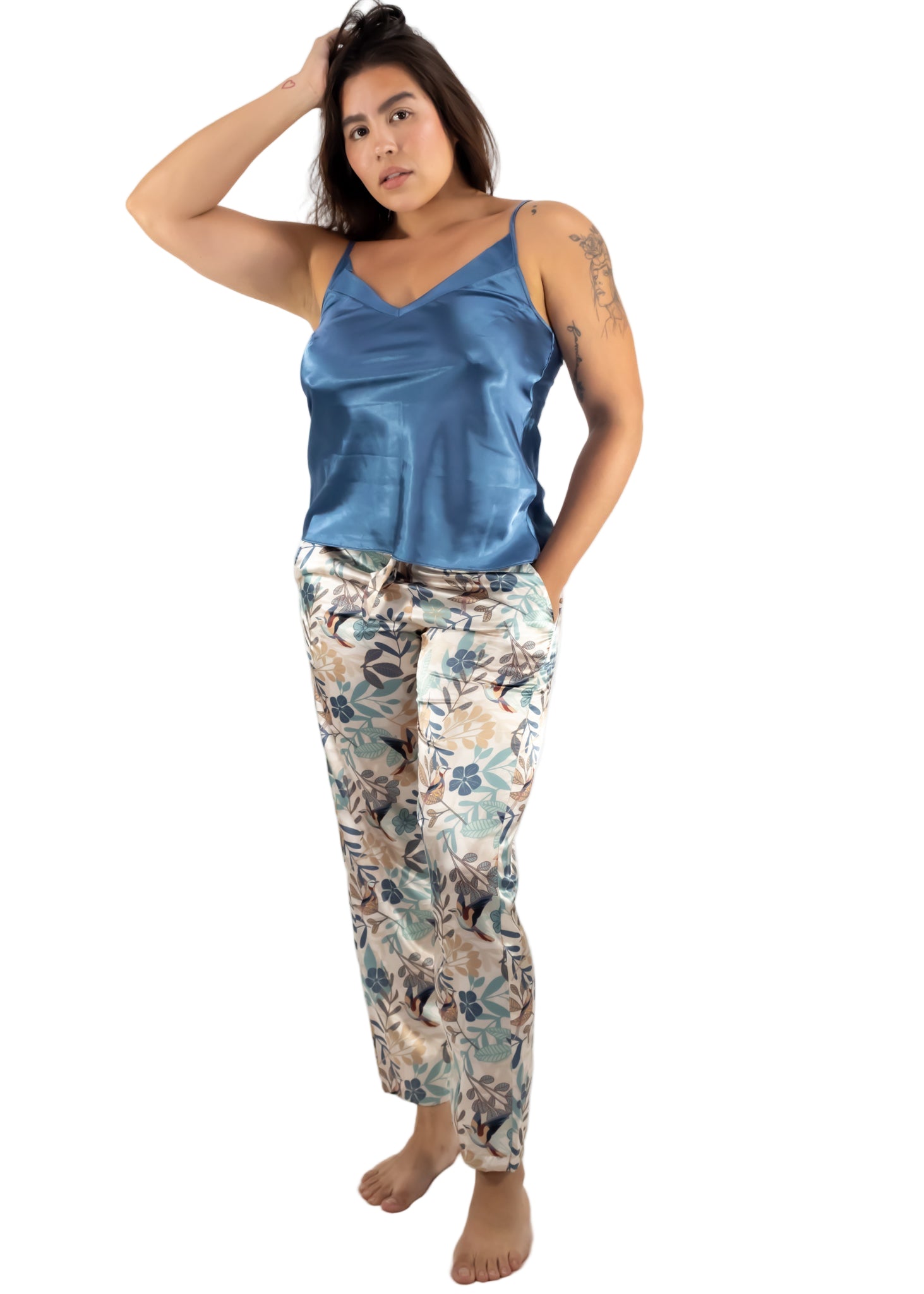 Woman wearing a blue satin tank top and floral pajama pants on a white background