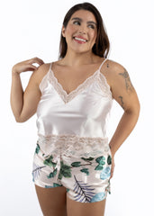 Woman wearing a beige satin camisole with lace trim and floral shorts on a white background