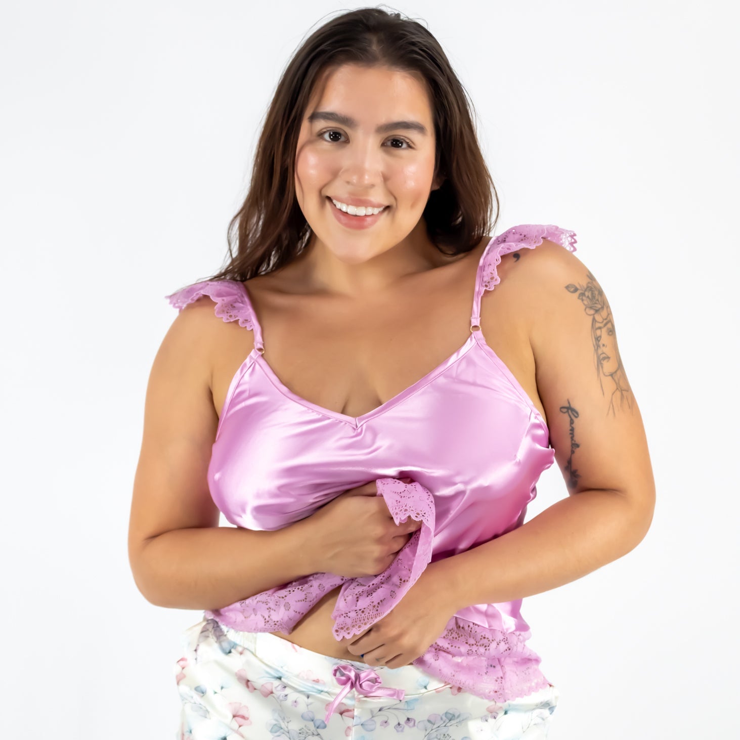 Woman wearing a pink satin top and white floral shorts on a white background