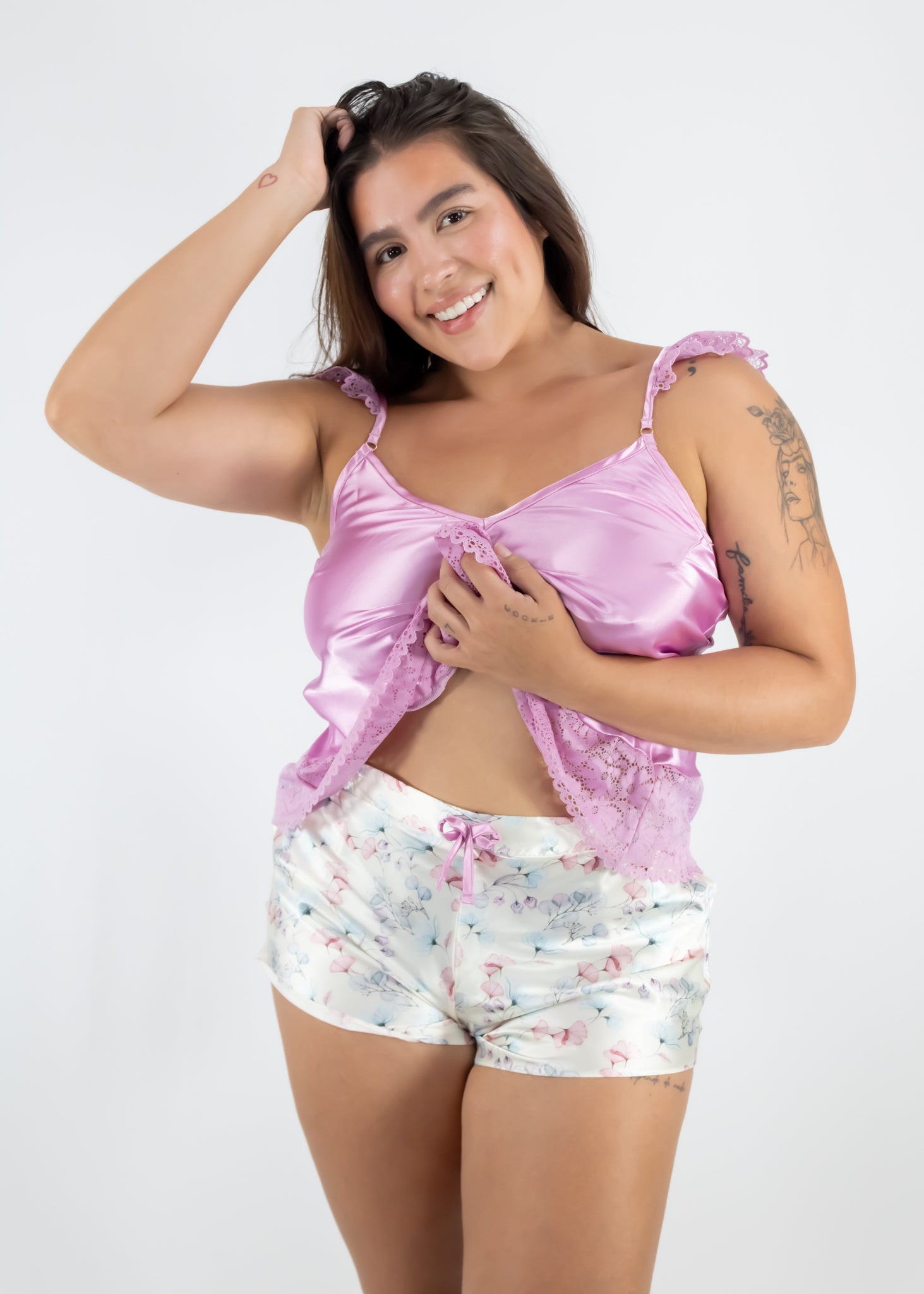 Woman wearing a pink satin top and floral shorts on a white background