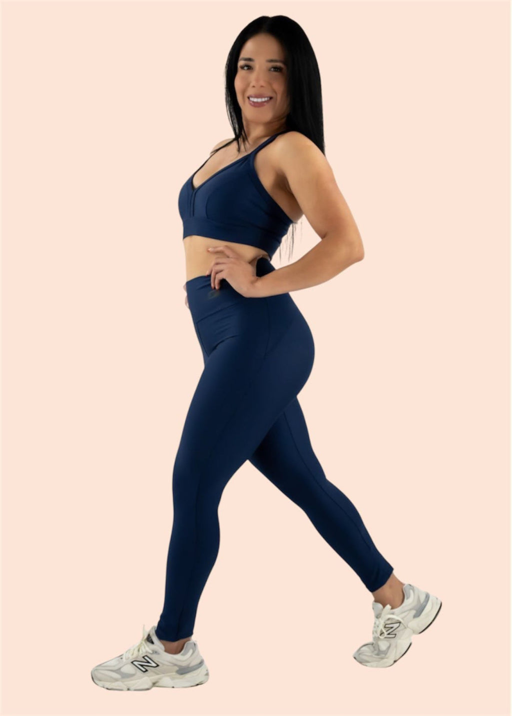 Woman wearing a navy blue sports bra and leggings set on a light pink background
