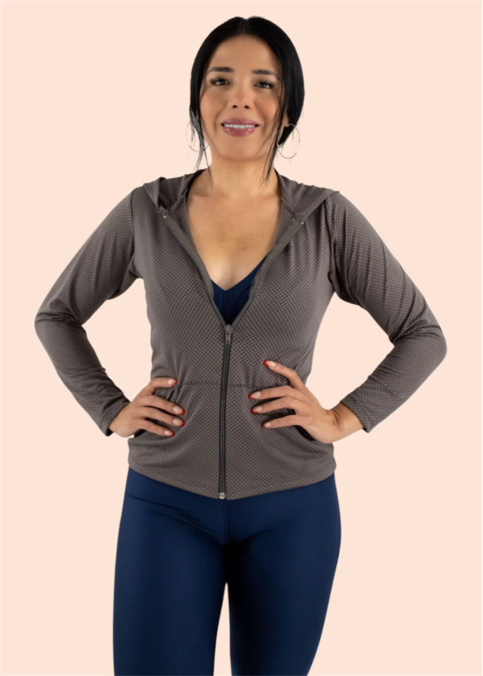 Woman wearing a gray zip-up hoodie and blue leggings on a beige background