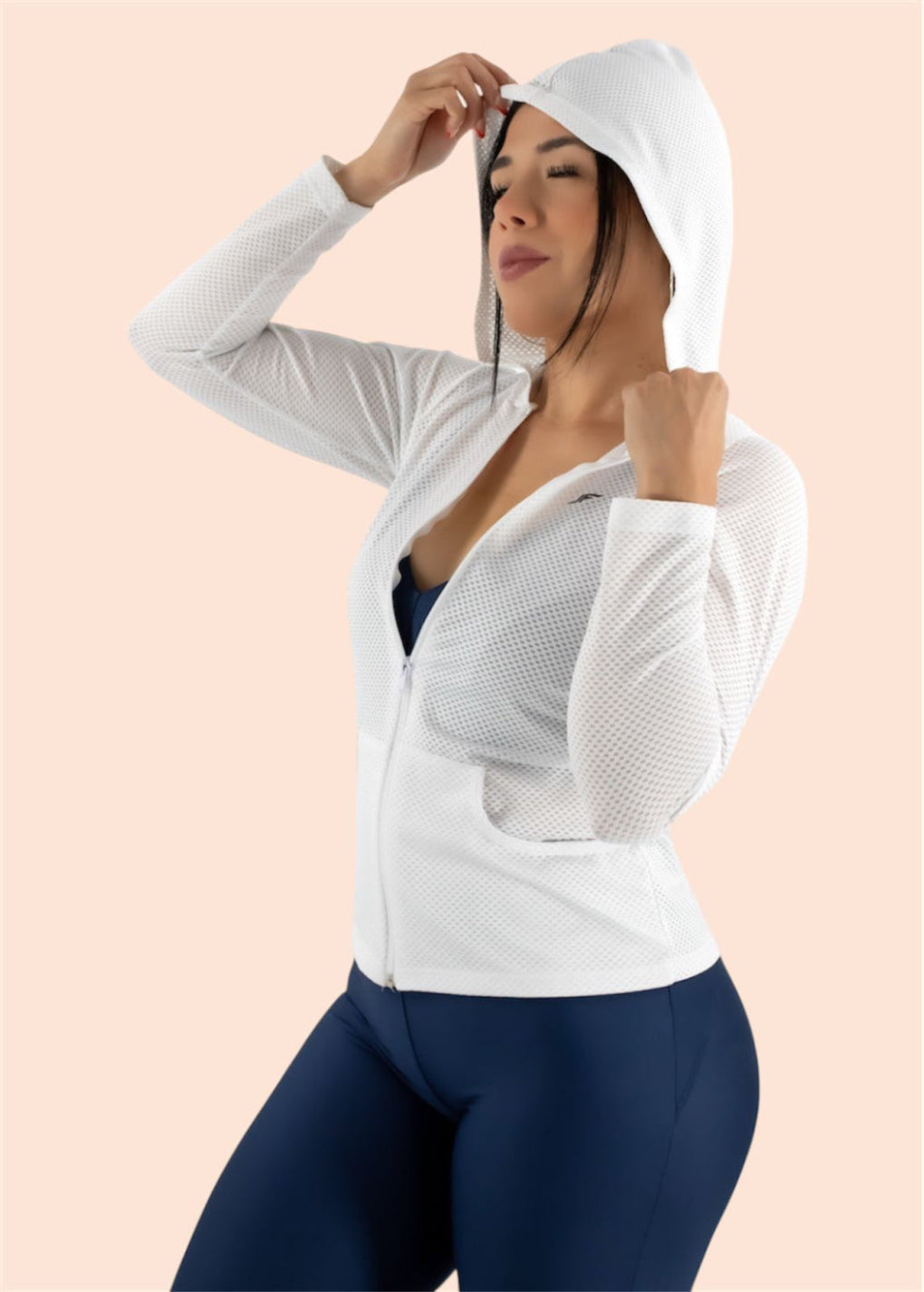 Woman wearing a white hoodie and navy leggings on a light pink background