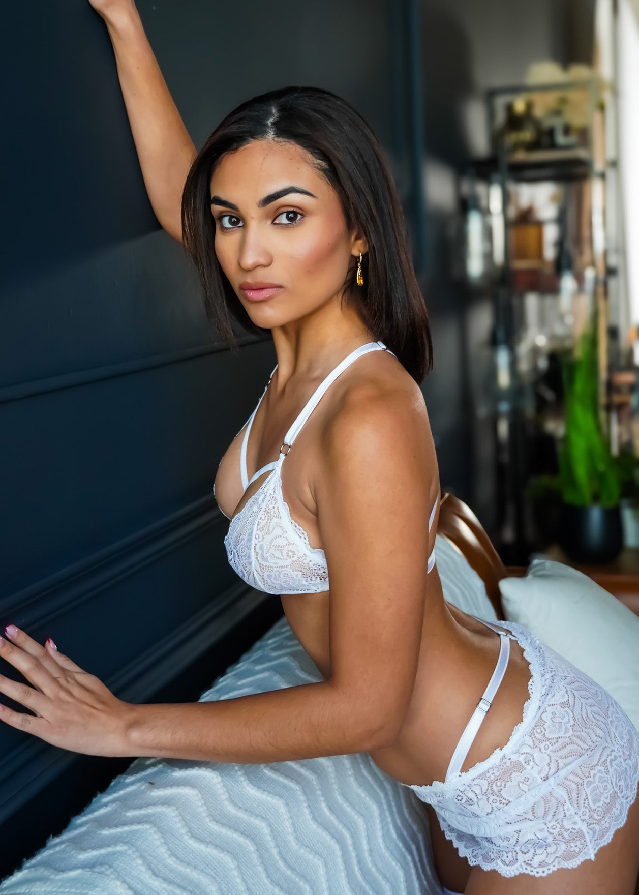 Woman in white lace lingerie sitting on a piano in a room with decor elements.